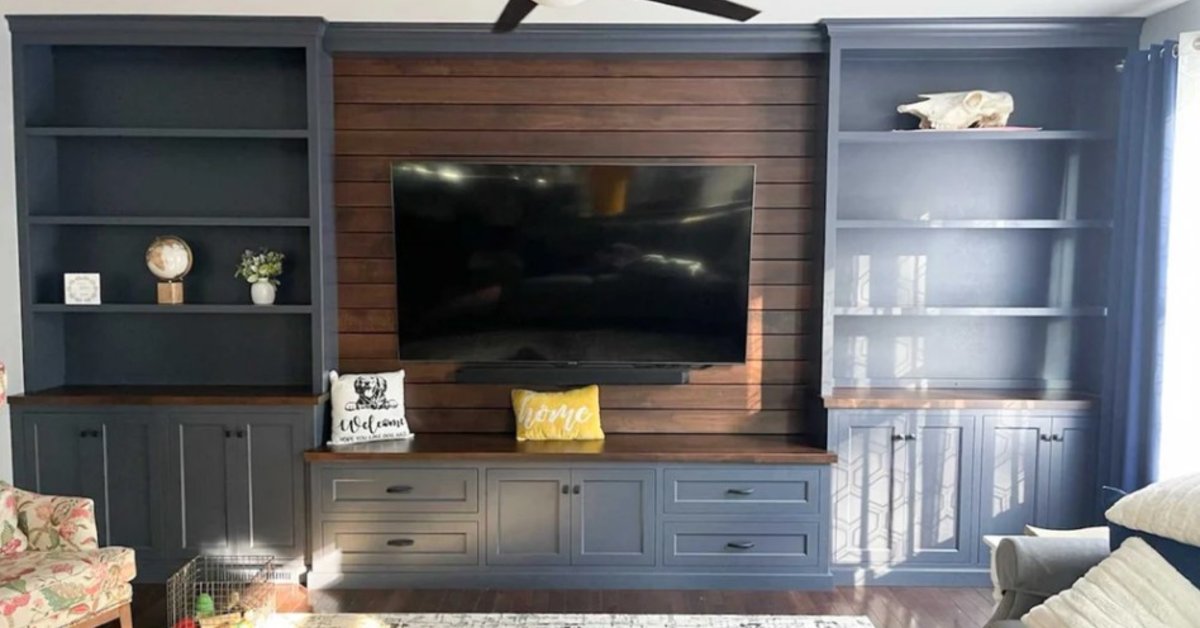 A built-in entertainment center with dark cabinetry, a wood accent wall, shelving, and a mounted television.