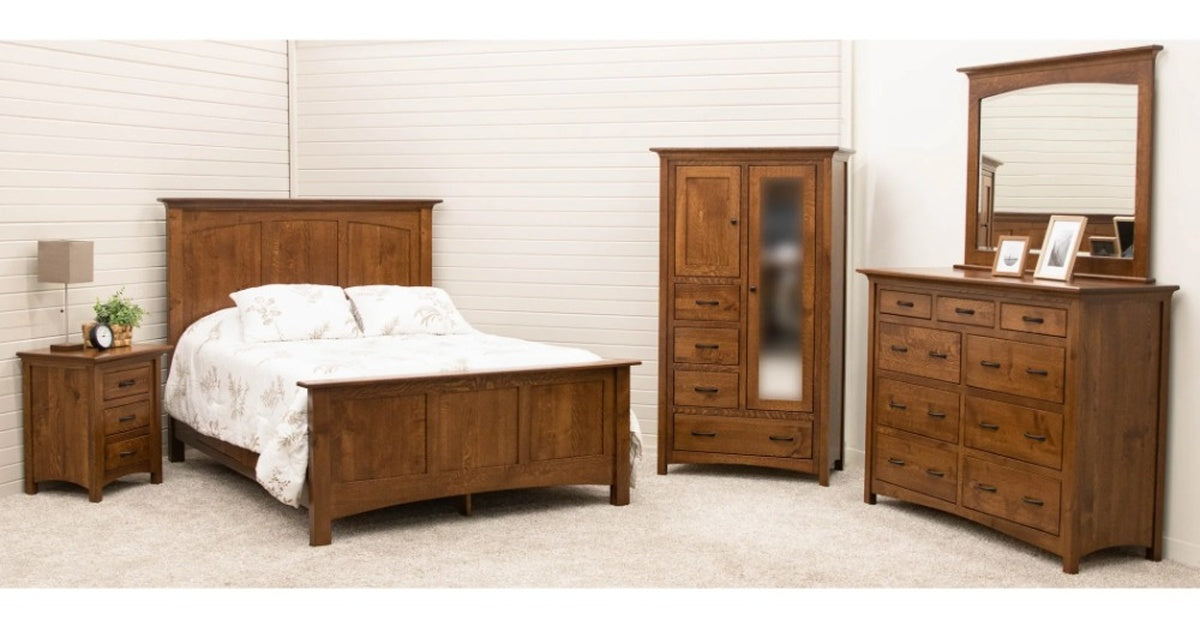 A bedroom with a wooden bed, nightstand, wardrobe, and dresser arranged on beige carpet against white walls.