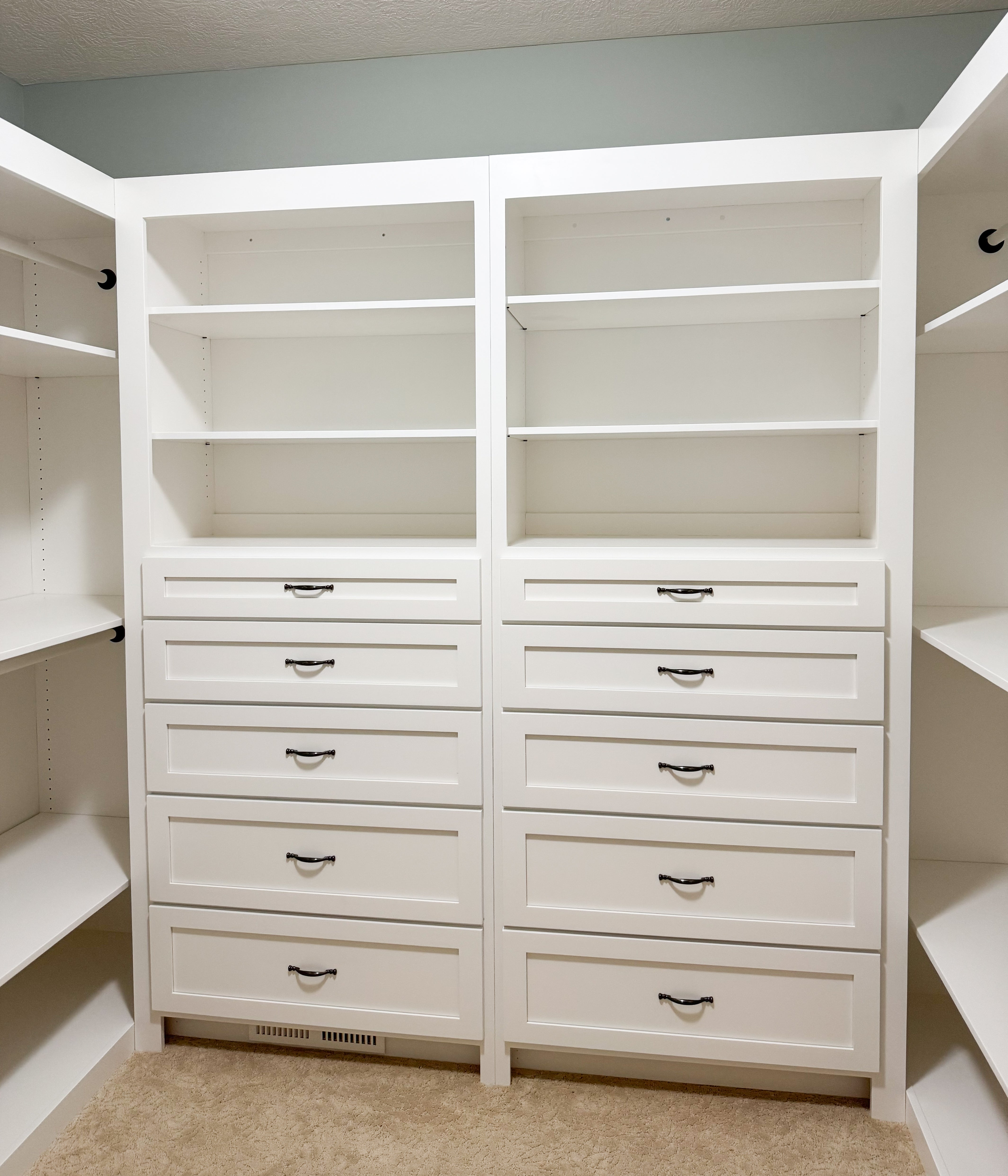 A built in wardrobe featuring white drawers and black hardware, in a clean, modern style.
