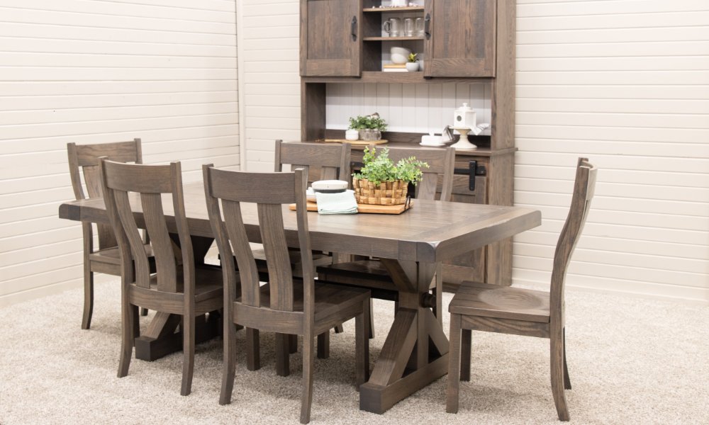 A wood dining table with matching chairs and a cabinet displayed on a carpeted floor against white paneled walls.